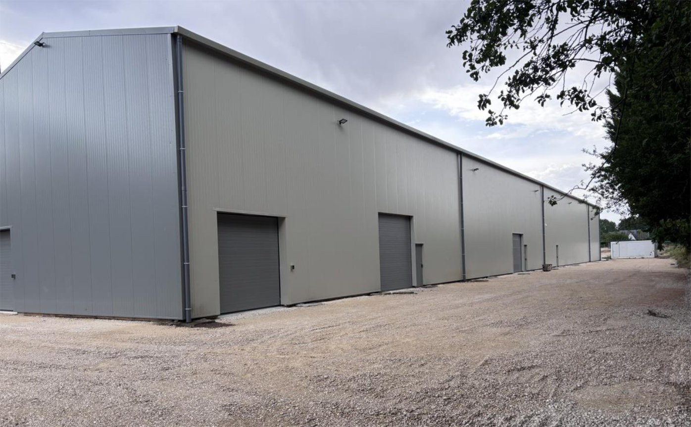 Un grand bâtiment de stockage moderne de Cerfbox avec plusieurs portes sectionnelles grises pour les box de stockage, situé sur un terrain en gravier.